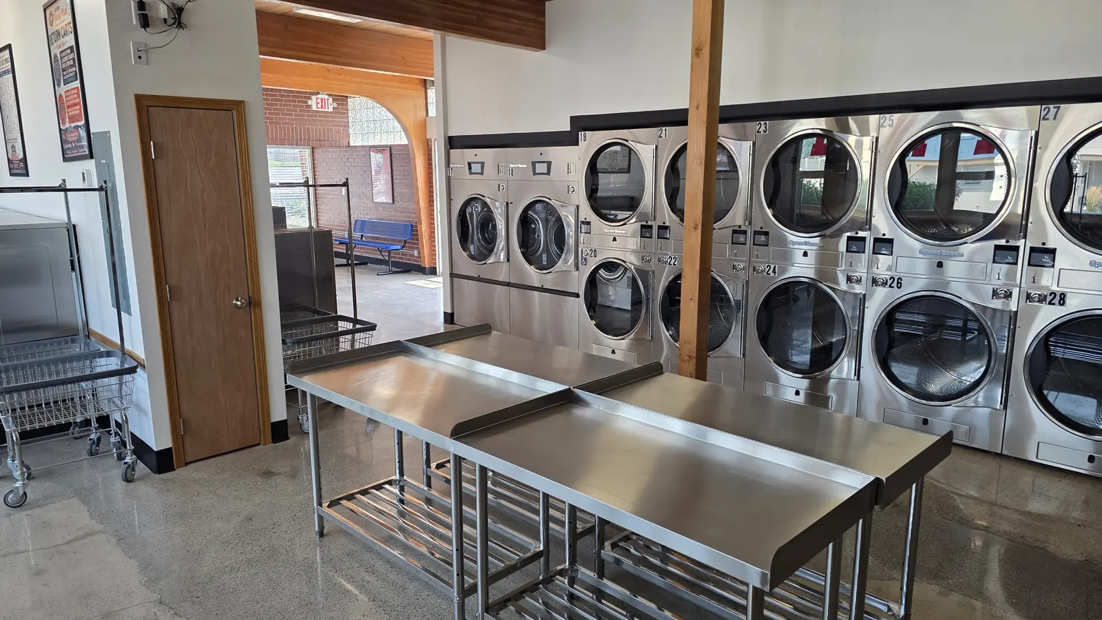 A wall of stacked 55 pound high-efficiency gas dryers with stainless folding tables in front of them