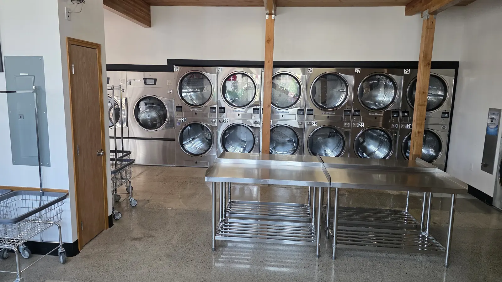 Numbered stacked dryers beside a long stainless folding table on polished concrete floor