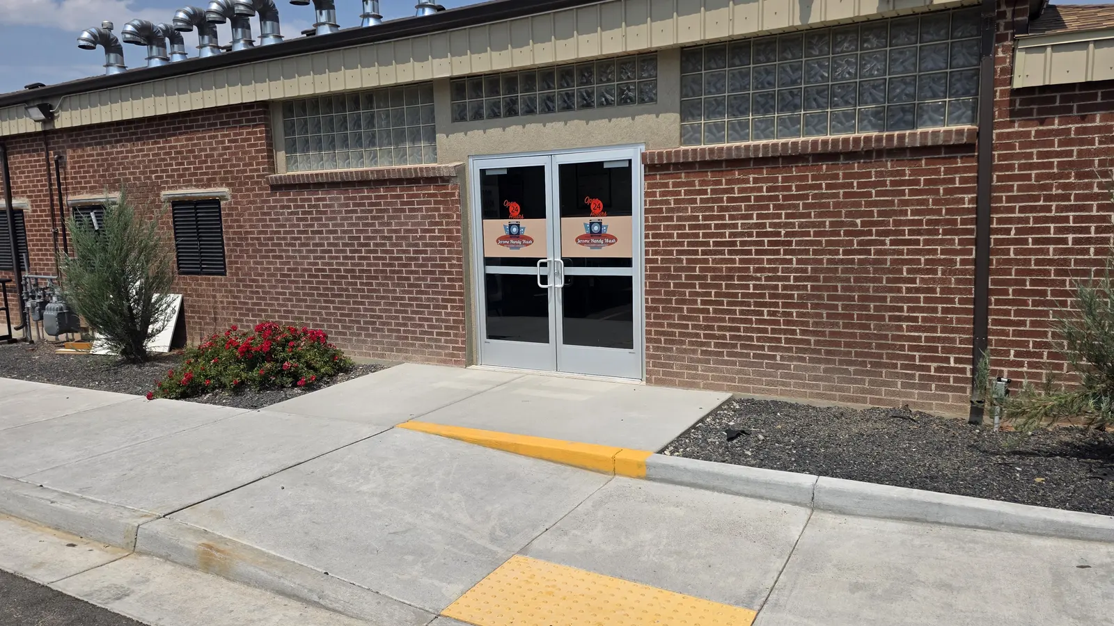 The double glass entrance doors at Jerome Handy Wash with a level concrete walkway and a yellow detectable warning strip at the curb