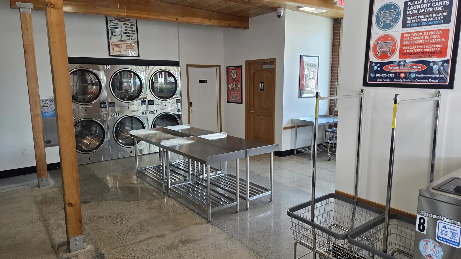 Stainless folding tables and rolling laundry carts under a bilingual please return carts sign