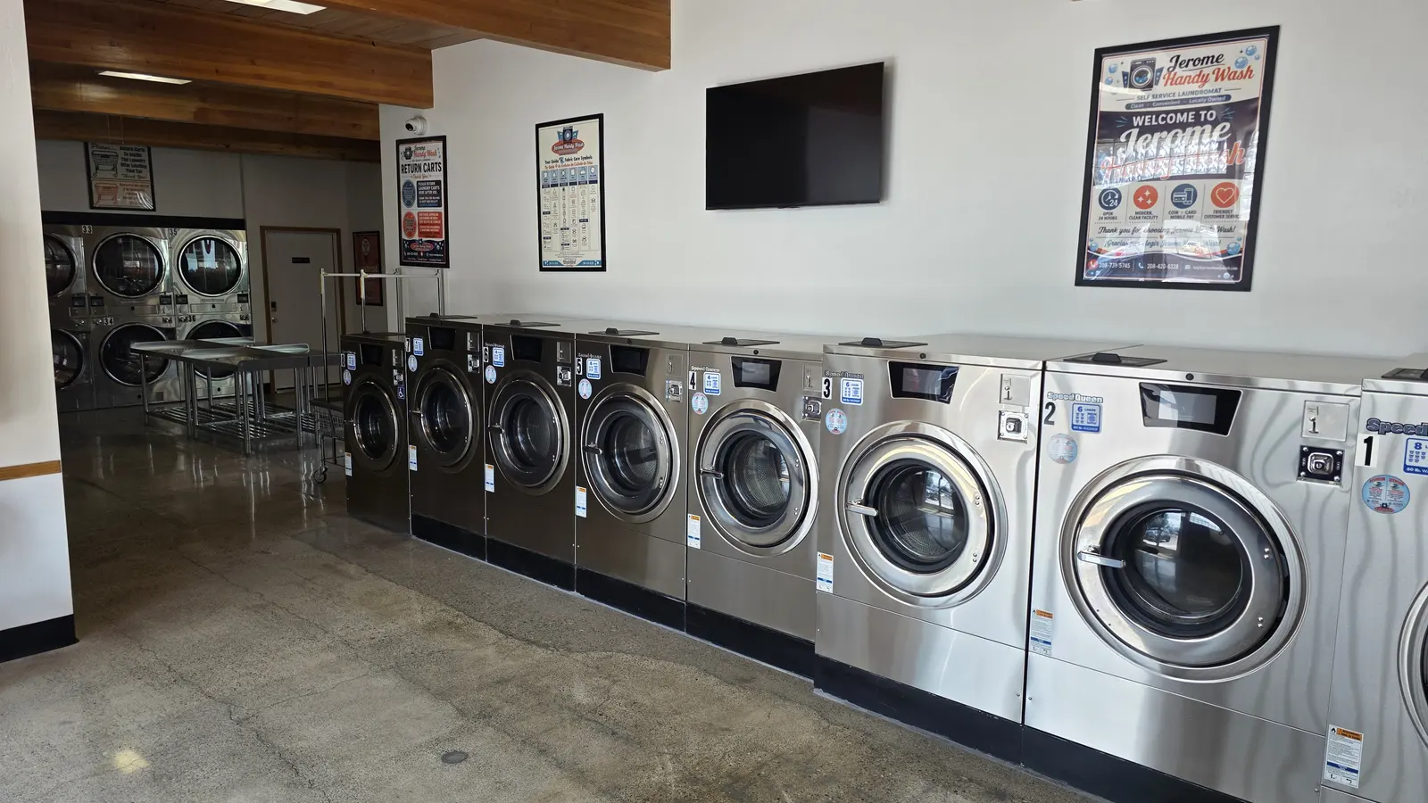 Inside Jerome Handy Wash, a long row of stainless Speed Queen washers running down one wall with stacked dryers and stainless folding tables at the far end