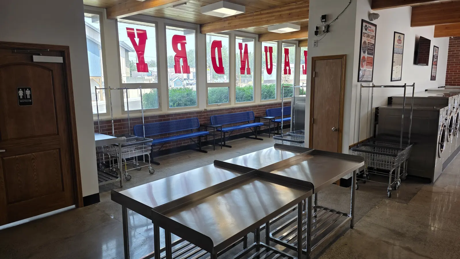Blue benches along a window wall with the word laundry in large red letters on the glass, and a restroom door to the left