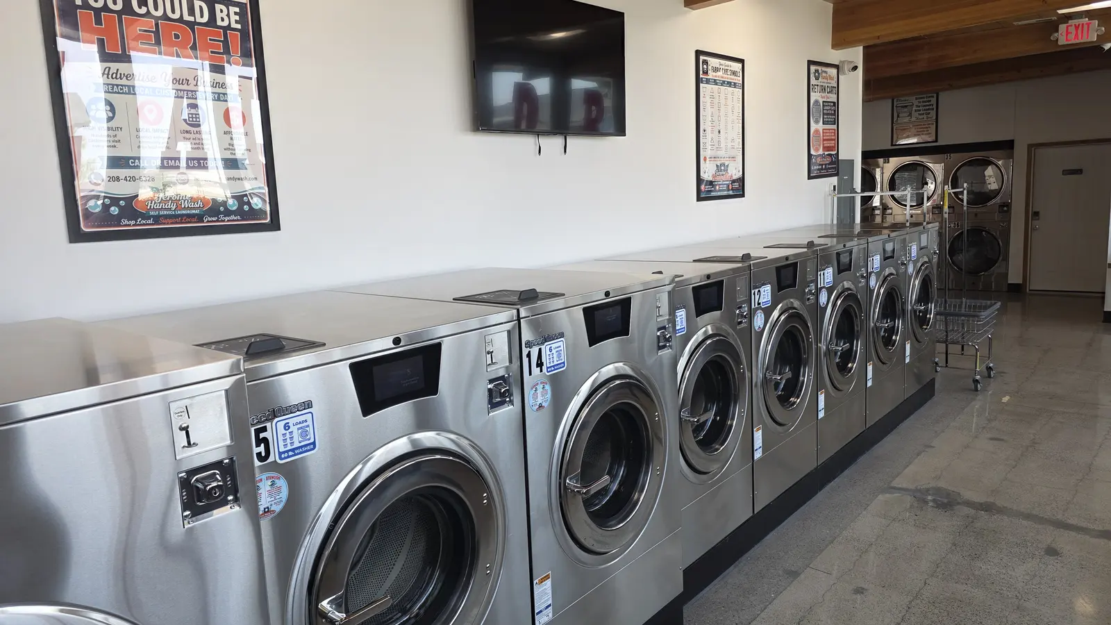 Washers and stacked dryers seen from the front of the store, with a television and framed information posters on the wall